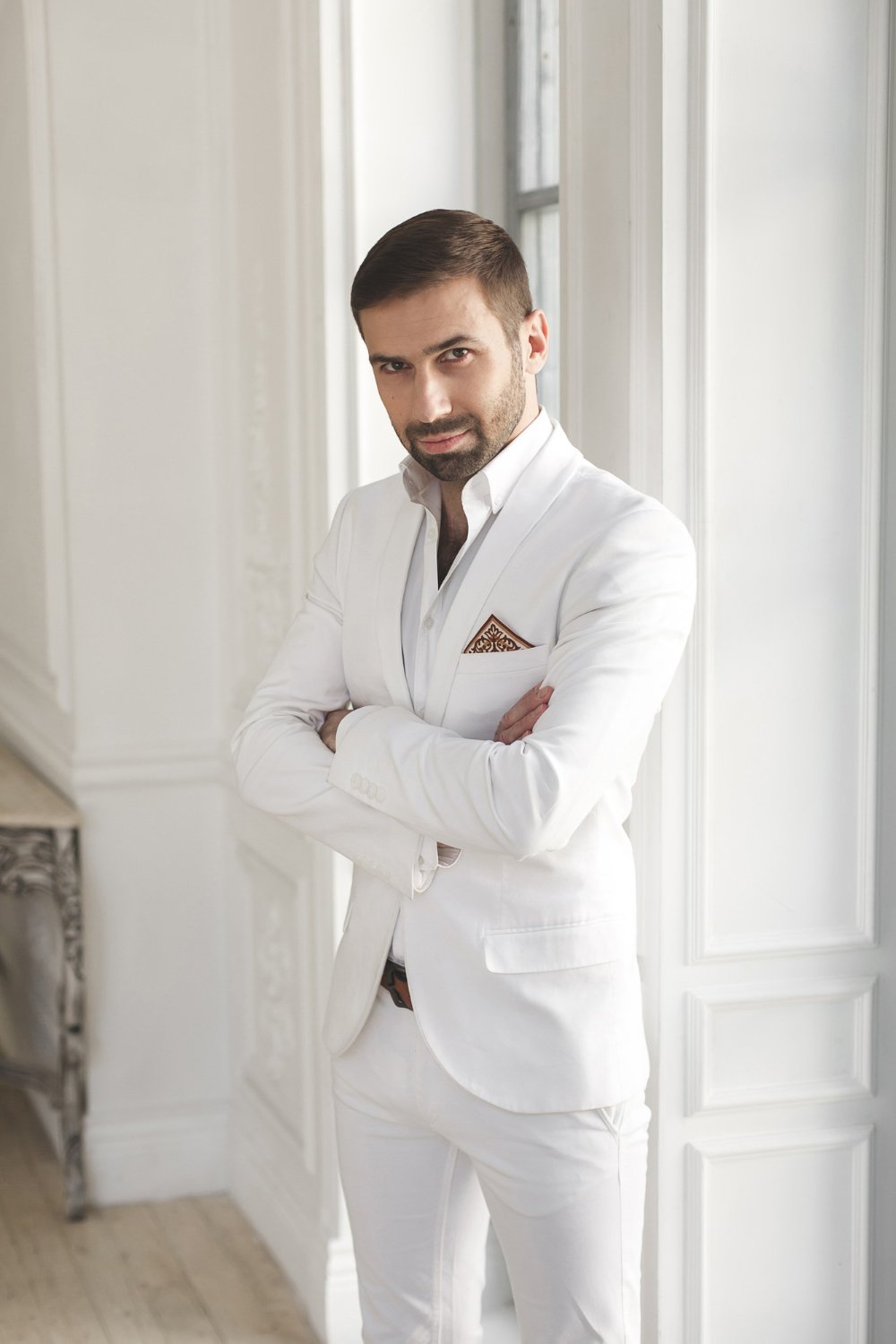 elegant young handsome man with a beard in a white classic suit